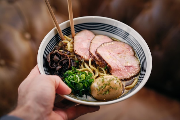 De cima da colheita mão anônima de pessoa mostrando delicioso ramen com pauzinhos em um restaurante asiático