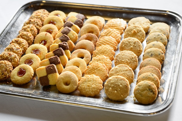 De cima de saborosos biscoitos doces feitos à mão colocados em uma bandeja de prata na mesa branca durante o dia