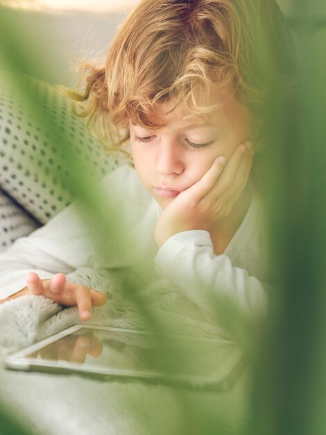 Foto de cima de um menino pré-adolescente focado tocando na tela do tablet enquanto navega pela internet em casa