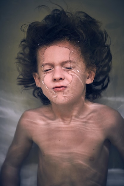 De cima de uma criança bonitinha com os olhos fechados mergulhando debaixo d'água enquanto tomava banho na banheira