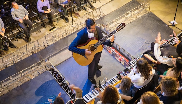 De cima, um músico masculino no palco a tocar guitarra com paixão cercado por um público imerso...