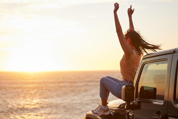 Dê graças aos presentes do universo. Foto de uma jovem comemorando uma vitória pessoal enquanto observa o pôr do sol na praia.