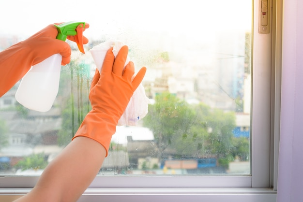 Dé a guantes la ventana de la limpieza con el trapo y el aerosol del limpiador en casa.
