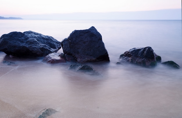 De manhã cedo na costa rochosa do mar. Água suave do mar por causa da longa exposição. Tempo de nascer do sol.