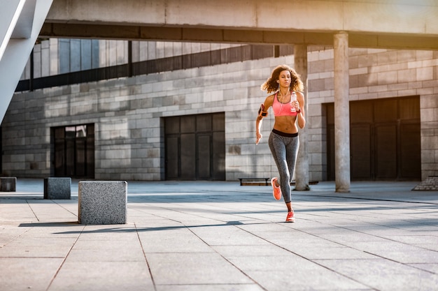 De manhã. Mulher atlética em forma correndo na cidade enquanto faz exercícios matinais