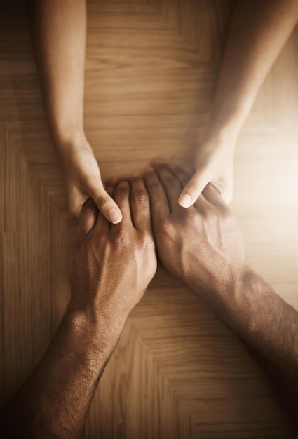 De mãos dadas, amor e apoio com as pessoas na mesa de madeira de cima para conforto ou empatia, ansiedade, depressão e confiança com amigos em casa juntos para ajuda em crise de dor, perda ou dor.