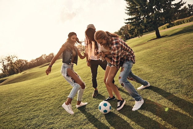 Foto dê-me a bola! comprimento total de jovens sorridentes em roupas casuais, curtindo um belo dia de verão enquanto jogam futebol ao ar livre