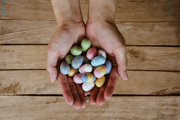 Dé la mujer que sostiene los huevos de Pascua coloridos en el fondo de madera de la tabla.