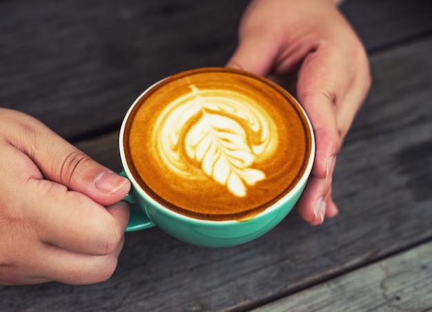 Dé a las mujeres con café del capuchino en una taza verde en de madera