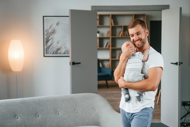 Foto de pé com o bebê nas mãos pai com criança está em casa cuidando de seu filho