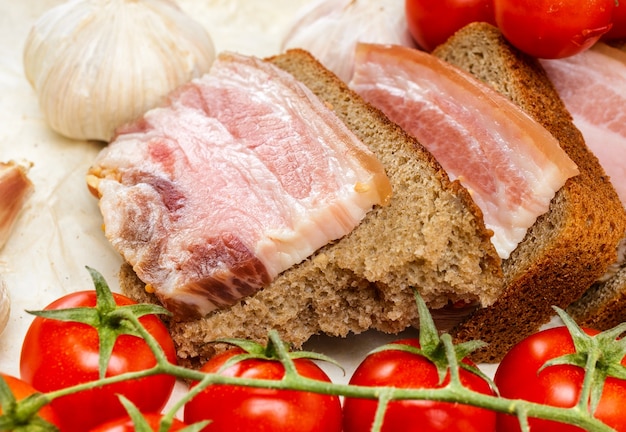 De sanduíches de bacon salgado no pão de centeio. Com tomate cereja e alho.