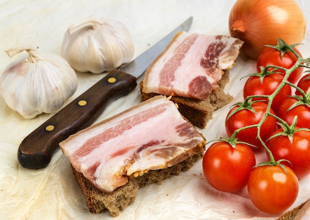 De sanduíches de bacon salgado no pão de centeio. Com tomate cereja e alho.