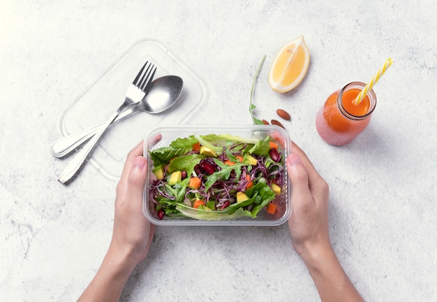 Dé sostener la caja de almuerzo fresca de la dieta sana con la ensalada vegetal en fondo de la tabla.