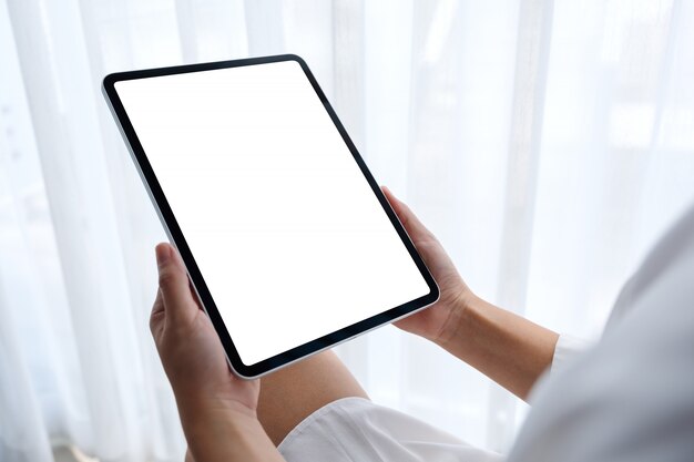 De uma mulher segurando preto tablet pc com tela branca em branco, enquanto está sentado no quarto com a sensação de estar relaxado pela manhã