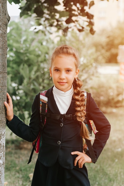 De volta à escola criança feliz aluno estudante oito anos de idade em uniforme de moda com mochila e penteado volumosa longa trança pronta indo para a segunda série primeiro dia na escola primária