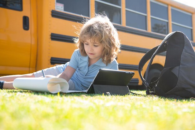 De volta à escola. Criança feliz, estudo no parque perto do ônibus escolar. Aluno fazendo lição de casa ou educação online ao ar livre.