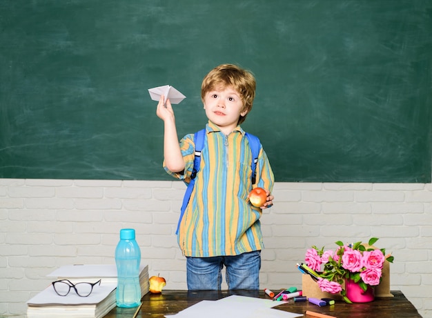 De volta à escola e aula de origami feliz na escola, garotinho brinca com uma criança de avião de papel