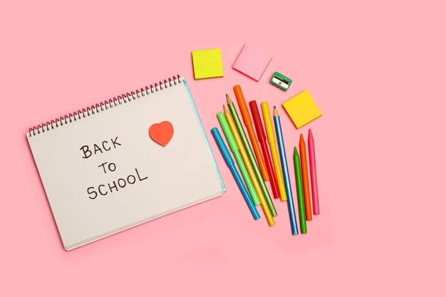 De volta à escola, escreva em um caderno, lápis de cor e marcadores em um fundo rosa com espaço de cópia