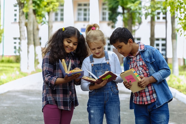 De volta à escola. Feche três amigos com mochilas, abraçando e rindo na frente da escola. Grupo racial misto de crianças da escola se divertindo no pátio da escola.