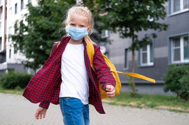 De volta à escola Garota usando máscara e mochilas protege e segura contra coronavírus Criança indo para a escola após pandemia Olhando para a câmera, os alunos estão prontos para o novo ano letivo