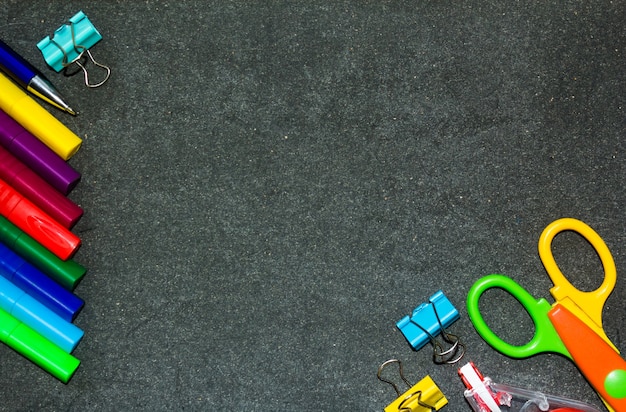 De volta à escola. Material escolar contra o fundo de um quadro escuro. Copie o espaço.