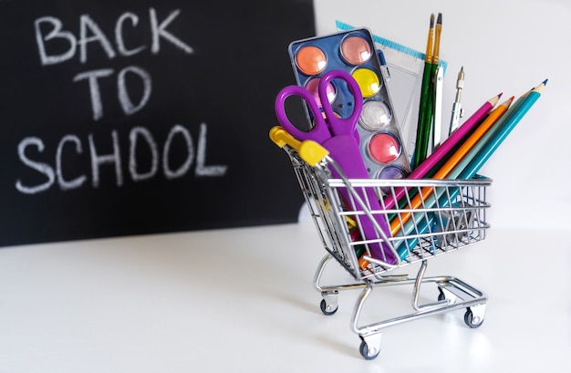 De volta à escola. Mini carrinho de compras com lápis e material escolar em um fundo branco. Banner escolar