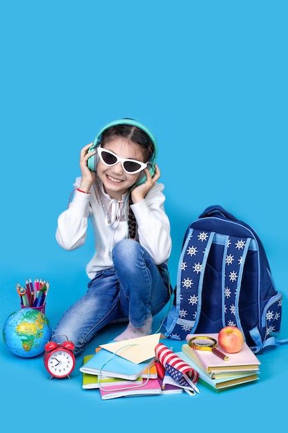 De volta à escola O retrato da menina da escola em óculos senta-se no chão sobre fundo azul