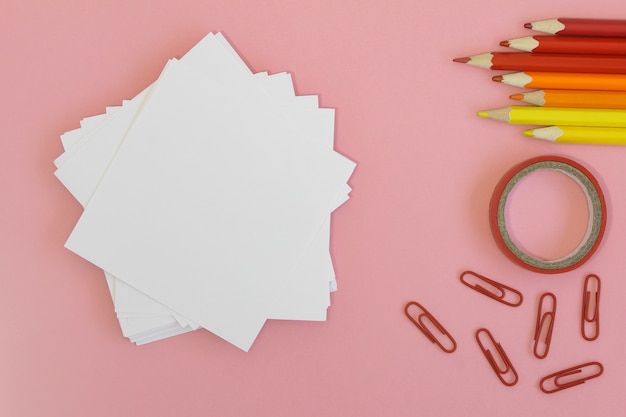 Foto de volta à escola . papel para escrever com lápis, clipes e fita em um fundo rosa.