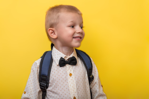 Foto de volta à escola um menino loiro sorridente com uma mochila em um fundo amarelo olha para longe opy space education banner