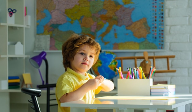 De volta à escola, um miúdo da escola primária sentado à secretária e a desenhar, um estudante a fazer a escola.