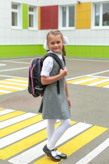 De volta à escola Uma menina com mochilas escolares vai para a escola sorri e olha para a câmera Uma criança caminha perto do jardim da escola ano novo para os alunos