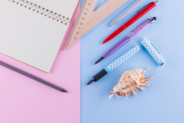 Foto de volta ao conceito da escola escritório escolar e conchas de mar em fundo rosa-azul pênis e lápis