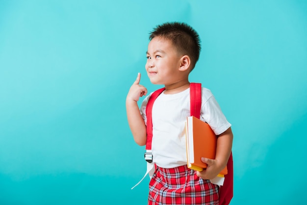 Foto de volta ao conceito de escola asiático feliz e engraçado garotinho sorri abraçando livros e apontando o dedo