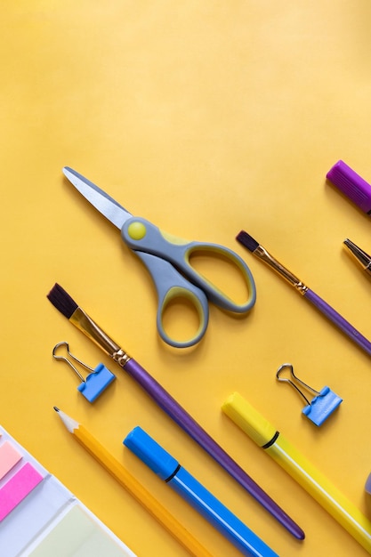 De volta ao conceito de escola Materiais escolares estacionários coloridos copiam espaçoVários itens de papelaria em um fundo amarelo Clipes de papel Clipes para pincéis de papel