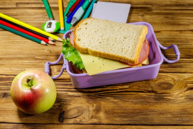 Foto de volta ao conceito escolar a escola fornece maçã e lancheira com sanduíches em uma mesa de madeira