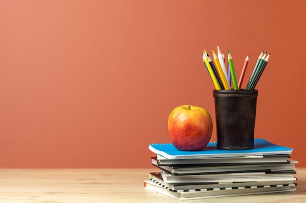 De volta às aulas Composição com elementos escolares lápis cadernos livros e maçã na mesa de madeira contra espaço de fundo marrom laranja para texto