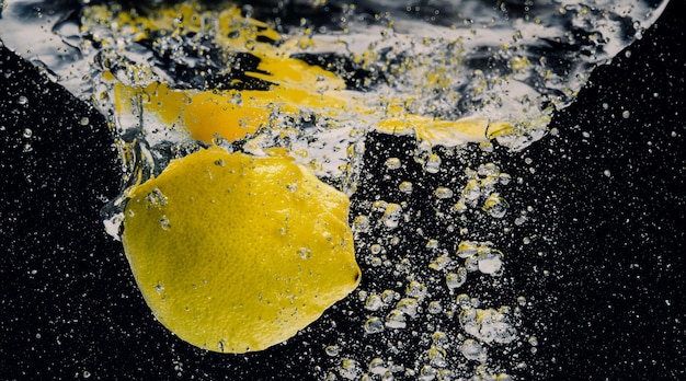 Foto debaixo d'água de limonada adoçada recém-espremida, que fatia de limão cru cai em água com gás contra um fundo azul escuro ou preto feche a limonada ou o coquetel de limão highball, bebida refrescante e fria