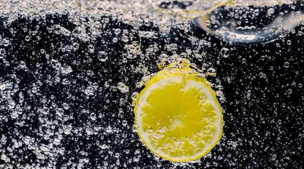 Foto debaixo d'água de limonada adoçada recém-espremida, que fatia de limão cru cai em água com gás contra um fundo azul escuro ou preto feche a limonada ou o coquetel de limão highball, bebida refrescante e fria