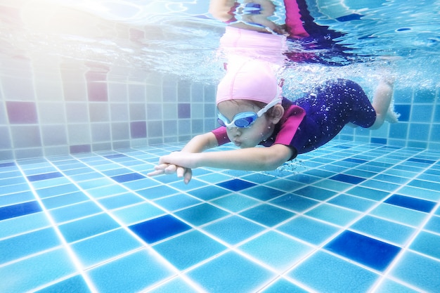 Foto debaixo d'água jovem menina bonitinha está nadando na piscina com seu professor de natação.