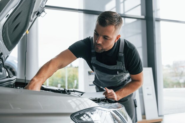 Foto debajo del capó, el hombre uniformado está trabajando en el autosalón durante el día