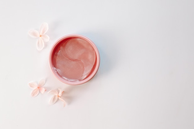 Debajo de los parches para los ojos en un frasco y flores sobre fondo blanco espacio plano para texto