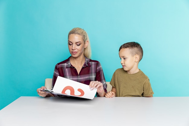 Deberes a distancia con la madre en casa en el momento de la cuarentena. Niño con mamá sentada en el escritorio y estudiando.