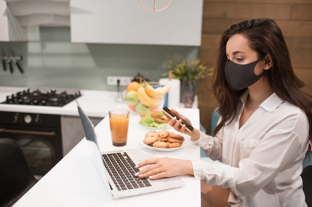 Debido a la pandemia de coronavirus, una mujer aislada en su hogar. Ella trabaja en casa, lleva una máscara y tiene una video conferencia en su computadora portátil.