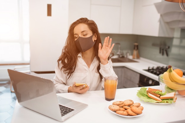 Debido a la pandemia de coronavirus, una mujer aislada en su hogar. Ella trabaja en casa, lleva una máscara y tiene una video conferencia en su computadora portátil.