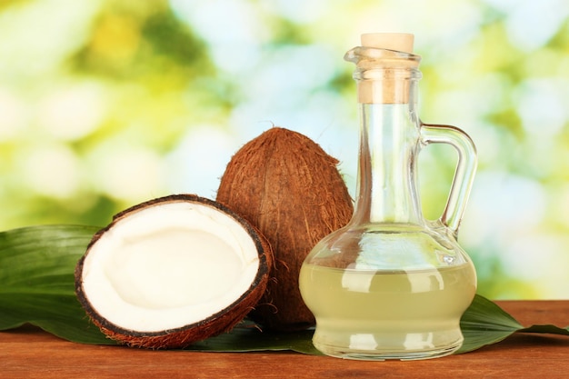 Decantador con aceite de coco y cocos sobre fondo verde