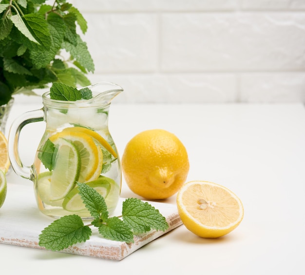 Decantador de vidro transparente com fatias de limão e folhas de hortelã em uma mesa branca desintoxicação Atrás dos ingredientes para a bebida
