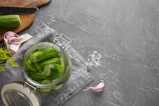 Decapagem e pepino de fermentação em frasco de vidro com endro e alho na mesa de concreta cinza escura. Fechar-se. Vista de cima.