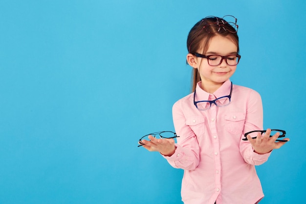 Foto decisión feliz y una niña con gafas de optometría aisladas en un fondo azul en el estudio