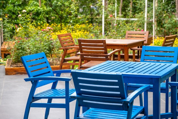 Deck, cadeira e mesa de madeira azul e marrom no jardim com fundo de campo de flores coloridas.