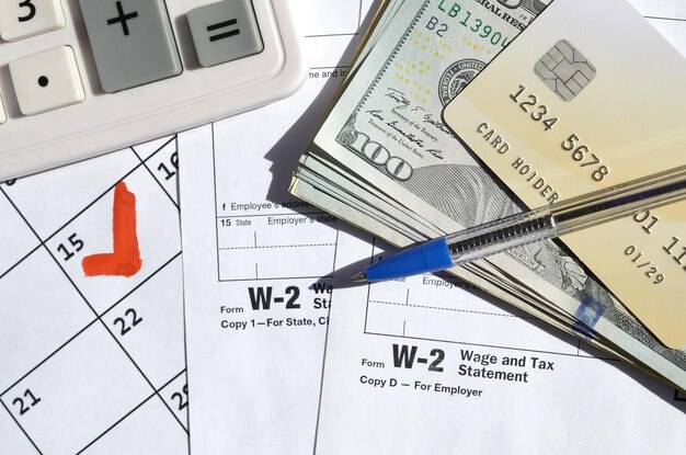 Foto declaração de salário e imposto w2 em branco com cartão de crédito em notas de dólar calculadora e caneta em página de calendário com marca de 15 de abril